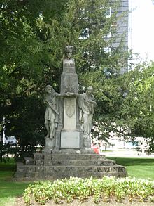 A monument on a park with a bust on top and two full-body figures on the sides.