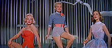 梦露于《愿嫁金龟婿》。她穿着橙色泳装，旁边是穿着短裤和衬衫的贝蒂·格拉布尔和身穿蓝色连衣裙的劳伦·白考尔。