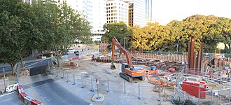 Construction site with an excavator sitting there. The station box has begun to be excavated.