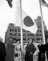 A group of men and women watching a flag being raised.