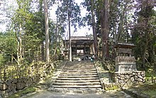 Staircase leading to a wooden roofed gate. Trees on either side of the staircase.