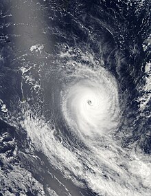Satellite image of a well-defined tropical cyclone, with a large central mass of white clouds surrounding a small void of clouds. Two small islands are visible at the image's left.