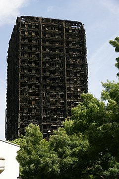 A tower block (Grenfell Tower) burning on nearly all floors with large amounts of smoke rising, and water being sprayed at the building from firefighters.