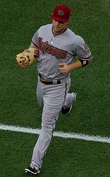A man in a grey baseball jersey and red hat with a script "D".