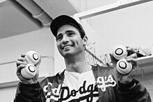 "a man dressed in a baseball uniform smiles for the camera while holding four baseballs, two in each hand."