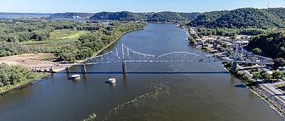 Summertime overlooking a wide and winding river. A small town is to the right. An old steel cantilever-truss bridge dominates the foreground.