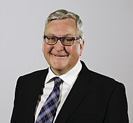 A close-up image of Fergus Ewing, a smiling 60-year-old man with short grey hair, glasses and a tartan tie