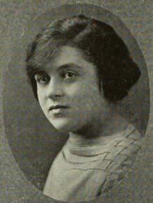 A young white woman with dark hair, wearing a top with a woven shoulder detail