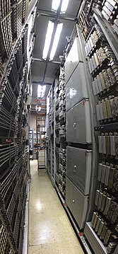 A vertical panorama showing tall aisles of equipment. On the right is a framework containing five large metal enclosures with access doors for each on the front.