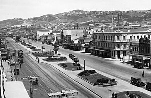 A black and white photograph of two urban streets with a strip of grass and walkways between them, with a statue of Queen Victoria on the divider.