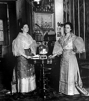 Two Mestiza Filipina women in traditional attire standing next to a table