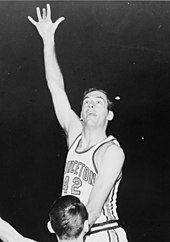 A basketball player attempts a jump shot with one arm outstretched. He is wearing a white jersey with "PRINCETON" and "42" in the front.