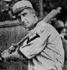 A man in a light, striped baseball uniform holding his bat on his shoulder.