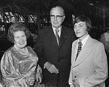 Anatoly Karpov, Max Euwe, and Max Euwe's wife Caro Bergman posing for a photo together. Karpov and Euwe are wearing business suits and ties, while Bergman is wearing a silken shirt and a pearl necklace.