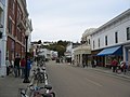 The downtown of a small town, showing many buildings, some pedestrians and a horse-drawn wagon.