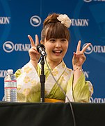 A smiling Ai Nonaka in costume, gesturing to an audience
