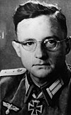 A man with glasses wearing a military uniform with an Iron Cross displayed at the front of his uniform collar.