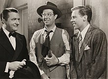 three men in suits standing in from of a brick wall.