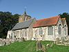 Stone church, the chancel roofed in red tiles the nave in slates, at the far end rendered tower surmounted by a small spirelet