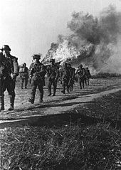 Several soldiers walking away from a burning house.