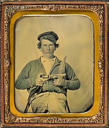 Sepia-toned photo of a young man holding a pistol.