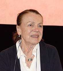 Iva Janžurová wearing a white blouse and dark cardigan, talking and looking left of camera