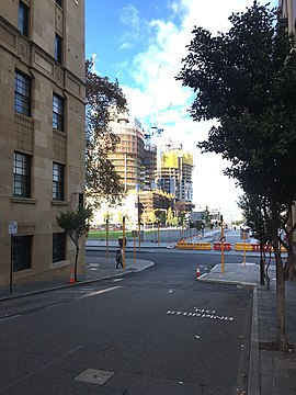 Tall buildings under construction beyond a cross-street, with buildings on side of current street in foreground
