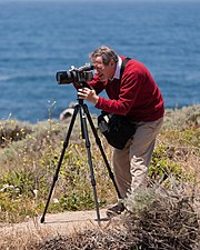 A photographer (Douglas Osheroff) setting up a shot with the aid of a tripod.