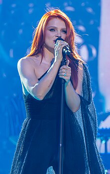 A redheaded female singing to a microphone dressed in black.