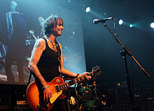 Robertson onstage holding his guitar and smiling