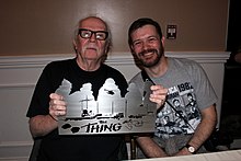 Carpenter holding a metal sign with a smiling fan