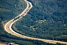 Aerial view of a divided highway making two turns in a densely forested area.