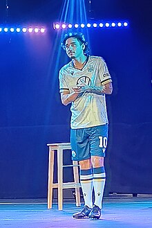 Man dressed in a football jersey standing up on a stage and clapping