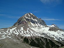 A rocky, pyramid-shaped mountain peak towering above lightly snow-covered rocky slopes.
