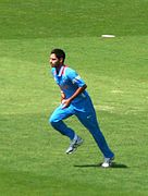A man wearing blue indian jersey and in bowling action.