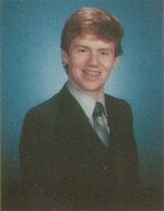A teenage boy wearing a black suit with a blue tie smiles.