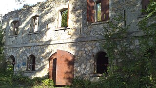 The façade of a ruined two-storey building with a large double metal door.