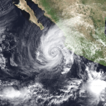 A satellite image of a hurricane approaching the west coast of Mexico; its eye is surrounded by convection spiraling inwards, and there is a large region of clouds fanning out to the north