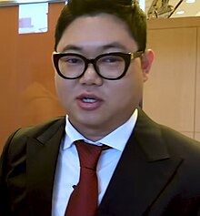 Photograph of Gamst wearing a suit, red tie, and reading glasses