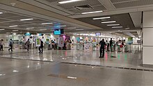 The concourse level of the station with the passenger service centre on the left. People are walking through the fare gates, some tapping their cards to enter or exit.