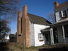 Photo of the one and one-half-story white wooden building with double brick chimneys.