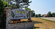Sign and flowers in a brick planter. Sign reads "established 1904, Dent welcomes you," and has images of two corn cobs.