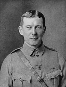 Upper body of a man in a soldier's uniform. He has short dark hair parted in the middle and maintains a neutral expression.