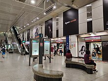 Photograph of NEL station platforms, with curved seats, station information signages and an escalator leading to the upper levels