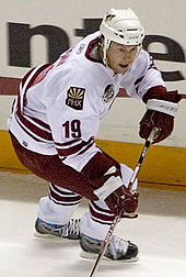 Doan skating, wearing hockey gear and holding a stick
