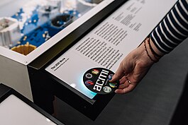 A round, black, disc-shaped card being tapped on a text label on a display inside a museum