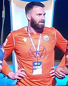 Bearded man in an orange jersey standing straight, hands on his hips