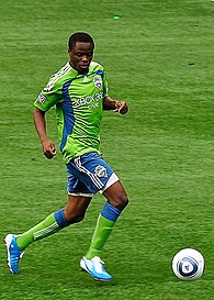 footballer in green and blue dribbles a ball down the field