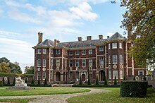 A photograph of the front of the house, showing a brick building with a circular drive in front of it