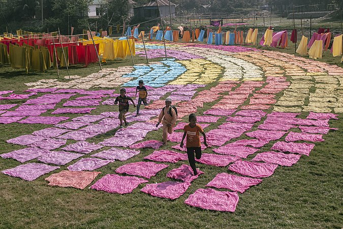 圖為在正在曬乾中的各色布料中玩耍的孩子。